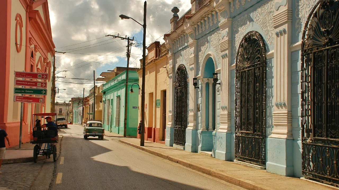 Brightly painted single-storey houses along a narrow street, with a pedicab parked at the kerb